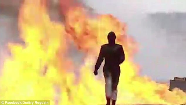 The masked figure doesn't even flinch as she steps confidently out of the fire